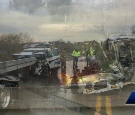 A police vehicle and a damaged SUV on a highway, with emergency responders attending to the scene. Dark clouds overhead create a somber atmosphere.