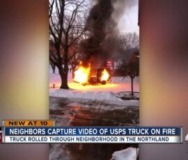 A postal truck engulfed in flames, with smoke rising, in a snow-covered neighborhood. Neighbors are visible in the background, recording the incident with their phones.